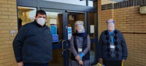 Three people outside a food bank with donated supplies in Witney